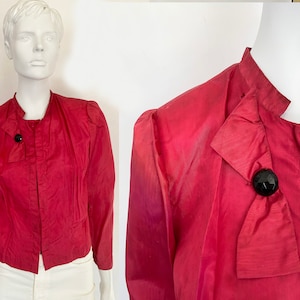 May include: A red silk jacket with a black button and a black bow at the collar.