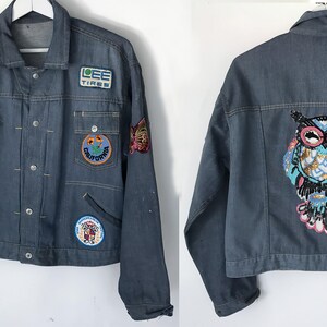 K&ouml;nnte beinhalten: Eine blaue Jeansjacke mit verschiedenen Patches, darunter ein Patch mit einer Eule mit Pailletten. Die Patches zeigen Bilder eines Berges, eines Reifens, eines Schmetterlings und eines Bikers.