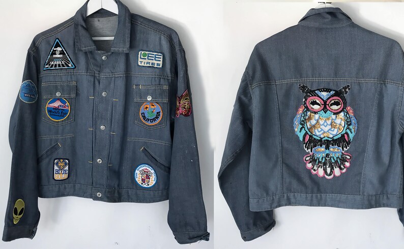 K&ouml;nnte beinhalten: Eine blaue Jeansjacke mit verschiedenen Patches, darunter ein Patch mit einer Eule mit Pailletten. Die Patches zeigen Bilder eines Berges, eines Reifens, eines Schmetterlings und eines Bikers.