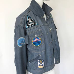K&ouml;nnte beinhalten: Eine blaue Jeansjacke mit verschiedenen Patches, darunter ein "Space Shuttle Hubble" Patch, ein "1974 World's Fair Spokane, USA" Patch, ein "White Pass" Patch und ein "Blue Gold" Patch.