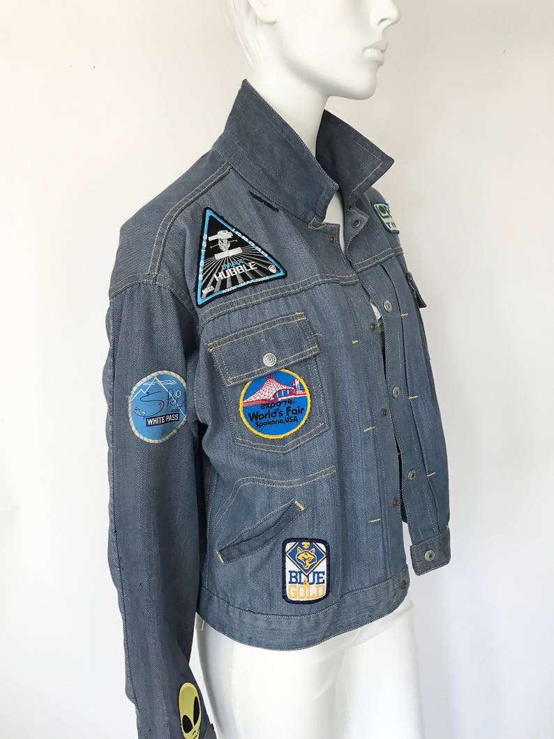 K&ouml;nnte beinhalten: Eine blaue Jeansjacke mit verschiedenen Patches, darunter ein "Space Shuttle Hubble" Patch, ein "1974 World's Fair Spokane, USA" Patch, ein "White Pass" Patch und ein "Blue Gold" Patch.