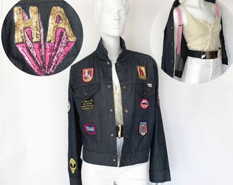 Könnte beinhalten: Eine dunkelblaue Jeansjacke mit verschiedenen Patches, darunter ein Pailletten-Patch mit der Aufschrift "HA", ein roter Patch mit einem Pferd, ein roter Patch mit einem Lippen-Design, ein blauer Patch mit einem "Goll"-Logo und ein rot-weiß-blauer Patch mit einem Stern-Design.