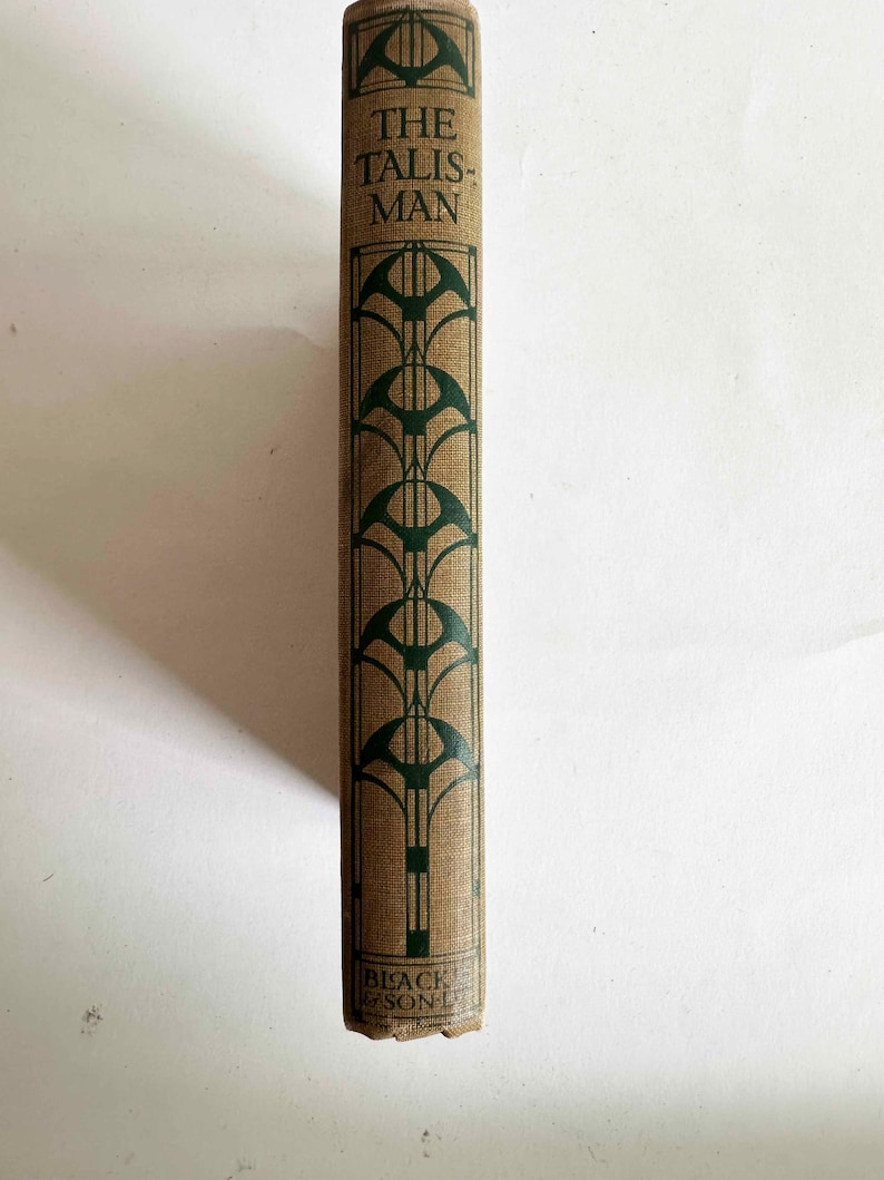 May include: A vintage book spine with the title "THE TALISMAN" in green lettering. The cover is tan with a repeating green art deco design. The publisher's name is visible at the bottom.