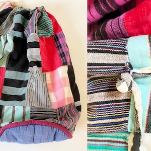 May include: A patchwork drawstring bag made from colourful striped fabric. The bag is made from a variety of fabrics, including red, blue, green, and black. The bag has a drawstring closure and is perfect for carrying small items.