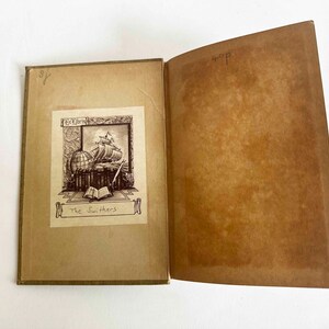 May include: Open vintage book with sepia-toned pages. The left page features a detailed illustration of a ship, globe, and books, with the title "The Swifters." The right page is blank. The book's cover is a light brown.