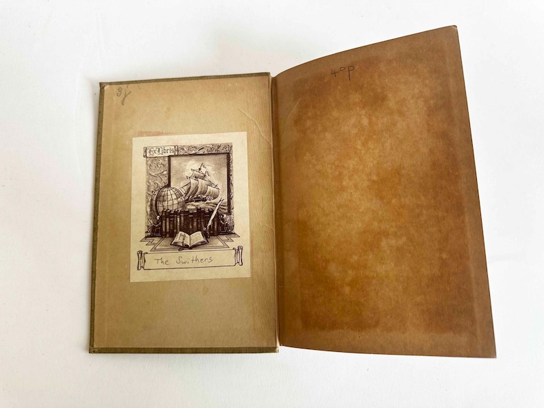 May include: Open vintage book with sepia-toned pages. The left page features a detailed illustration of a ship, globe, and books, with the title "The Swifters." The right page is blank. The book's cover is a light brown.