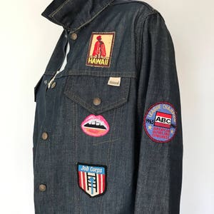 Peut inclure: Une veste en jean bleu fonc&eacute; avec divers patchs, dont un patch "Job Corps" rouge et blanc, un patch bouche rose et blanc, un patch "Hawaii" rouge et blanc et un patch rond avec le texte "1965 ABC 1966 American Bowling Congress League Champion".
