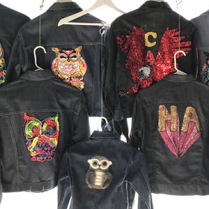 K&ouml;nnte beinhalten: Sieben Jeansjacken mit bunten gestickten Eulen-Patches auf der R&uuml;ckseite. Die Patches haben verschiedene Farben, Muster und Designs. Einige Jacken haben zus&auml;tzliche Verzierungen wie Pailletten und Glitzer.