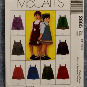 May include: McCall's sewing pattern for a child's dress, pattern number 2865, size CD (2-3-4). The pattern includes seven different dress styles, with various colors and patterns, including plaid, corduroy, and solid colors.