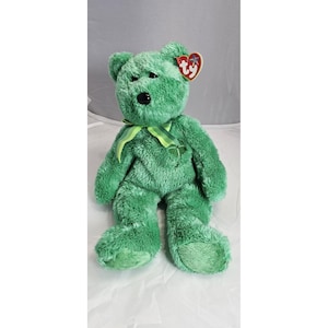 May include: A green plush bear with a shamrock ribbon and a Ty heart-shaped tag. The bear has a black nose and is made of soft, textured material. A collectible stuffed animal.