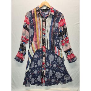 May include: A long-sleeved button-down shirt dress featuring a patchwork design with various patterns including floral motifs, geometric shapes, and vertical stripes in shades of navy blue, red, white, and yellow, with a collar and front button closure.