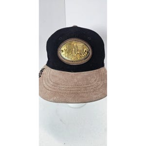 May include: Black and tan baseball cap with a gold-colored oval patch featuring a rocket, American flag, and text that reads "United States Space Program." The brim is tan, and the NASA logo is embroidered on the side.