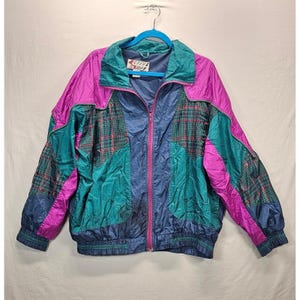 May include: A color-blocked windbreaker jacket featuring panels of magenta, teal, and navy blue. The jacket includes plaid patterned sections in teal, navy, and red, a full-length front zipper, and a label reading Active Stuff at the collar.