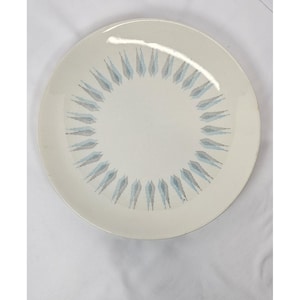 May include: A round, off-white ceramic plate with a decorative pattern. The pattern consists of a ring of stylized, light blue and gray feather-like shapes arranged around the plate's edge. The plate has a simple, elegant design.