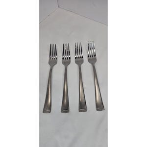 May include: Four stainless steel forks arranged in a row. Each fork has four tines and a long, slender handle. The forks are made of a shiny, silver-colored metal and are set against a white background. The forks are a classic design.