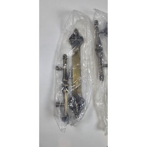 May include: Two sets of antique-style door hardware, each sealed in clear plastic. The hardware features a brass finish with ornate detailing, including decorative handles and hinges. The design suggests a vintage or classic aesthetic, suitable for home improvement projects.