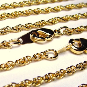 May include: Four gold rope chains with lobster claw clasps. The chains are arranged in a layered pattern, with the longest chain at the top and the shortest chain at the bottom.