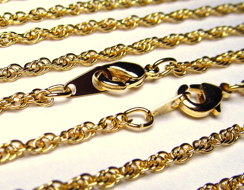 May include: Four gold rope chains with lobster claw clasps. The chains are arranged in a layered pattern, with the longest chain at the top and the shortest chain at the bottom.