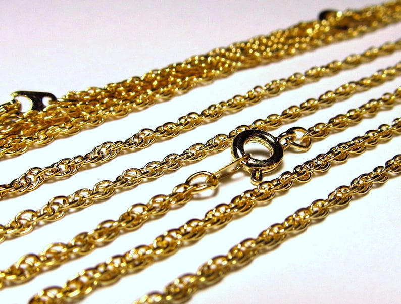 May include: Four gold chains of different thicknesses, with a clasp on one of the chains.