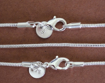 May include: Two silver snake chains with lobster clasps and round tags marked "925" on a brown surface.