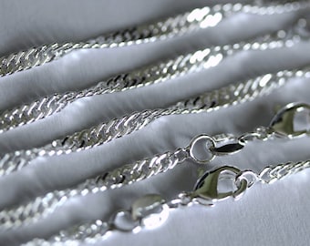 May include: Close-up of several silver-colored chain necklaces with lobster claw clasps. The chains have a twisted rope design, and the clasps are visible at the bottom of the image. The background is a soft, white surface.