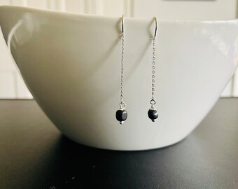 May include: A pair of silver dangle earrings with black square beads at the end of each chain.