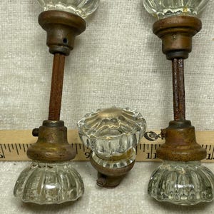 May include: Three antique glass door knobs with a clear, fluted design. The knobs are mounted on aged, rusty metal stems and bases. The hardware has a vintage aesthetic, suggesting a classic or retro style. The knobs are likely for interior doors.