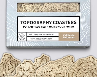 Peut inclure: Un ensemble de dessous de verre en bois clair avec des motifs de lignes de niveau complexes. La boîte d'emballage porte les inscriptions TOPOGRAPHY COASTERS, POPLAR + ECO-FELT + MATTE WOOD FINISH, SML | SIMPLE MODERN LIVING et California Volcanoes.