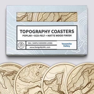 Könnte beinhalten: Ein Set aus Holz-Topographie-Untersetzern mit matter Oberfläche, verpackt in einer hellblauen Schachtel. Die Untersetzer zeigen detaillierte Konturlinien und den Text "TOPOGRAPHY COASTERS". Die Box enthält auch den Text "Yosemite Valley".