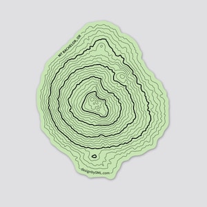 May include: A green and black topographic map sticker of Mt. Bachelor, OR. The sticker features a detailed contour map of the mountain with the text "MT BACHELOR, OR" and "designbySML.com" at the bottom.