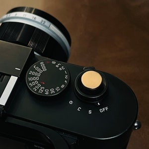 May include: A black camera with a silver lens and a dial with numbers from 8 to 4000. The dial is labeled with the letters A and B. The camera also has a dial with the letters C, S, and OFF.