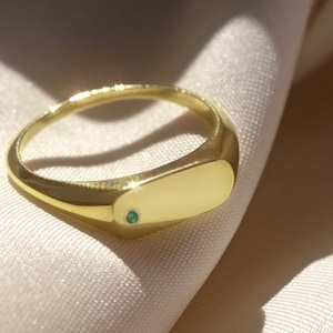 Puede incluir: Un anillo de sello de oro con una pequeña piedra preciosa verde engastada en el centro de la parte superior del anillo.