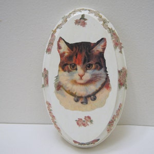 May include: White oval wooden plaque with a floral border and a vintage image of a cat with a bell collar.