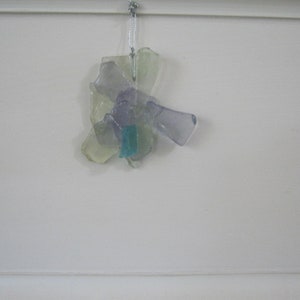 May include: A cluster of iridescent glass pieces in shades of purple, green, and blue, hanging from a white string. The glass pieces are arranged in a flower-like shape.