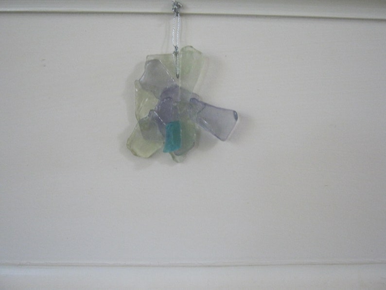May include: A cluster of iridescent glass pieces in shades of purple, green, and blue, hanging from a white string. The glass pieces are arranged in a flower-like shape.