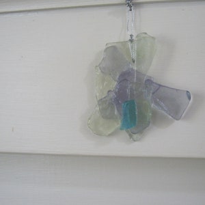 May include: A glass ornament made from multiple pieces of clear, purple, and blue glass. The ornament is shaped like a flower and hangs from a silver string.