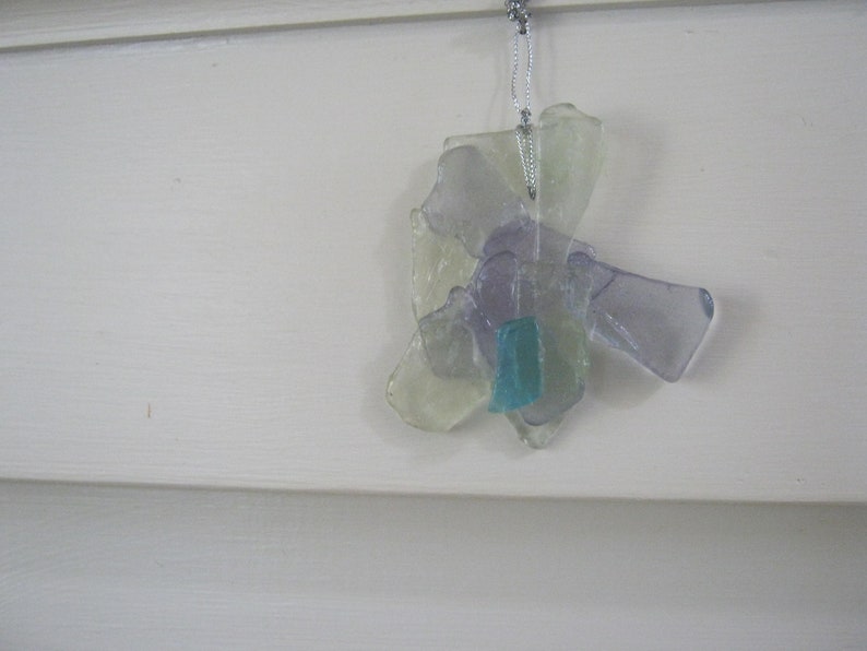May include: A glass ornament made from multiple pieces of clear, purple, and blue glass. The ornament is shaped like a flower and hangs from a silver string.