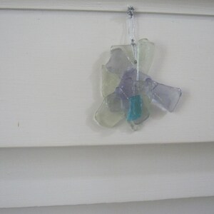 May include: A glass ornament shaped like a flower with purple and white glass pieces. The ornament has a blue glass piece in the center and is hanging from a silver string.
