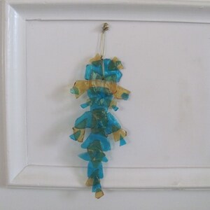 May include: A blue and gold iridescent ornament shaped like a seahorse hanging from a white wall.