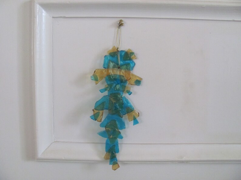 May include: A blue and gold iridescent ornament shaped like a seahorse hanging from a white wall.