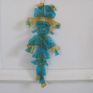 May include: A blue and gold glass ornament shaped like a seahorse. The ornament is made of many small pieces of glass that are glued together.