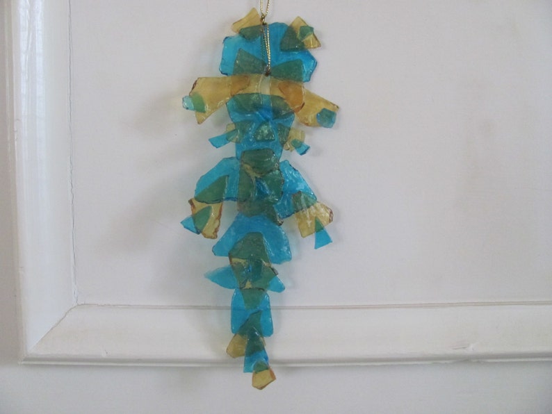 May include: A blue and gold glass ornament shaped like a seahorse. The ornament is made of many small pieces of glass that are glued together.