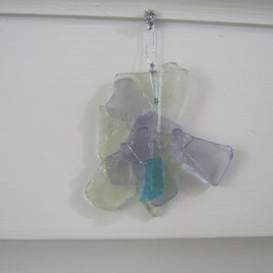May include: A glass ornament made of multiple pieces of clear, purple, and blue glass. The ornament is hanging from a silver string.