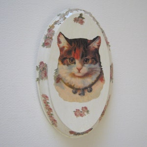 May include: A white oval ceramic plate with a floral design and a vintage image of a cat with brown, black, and white fur.