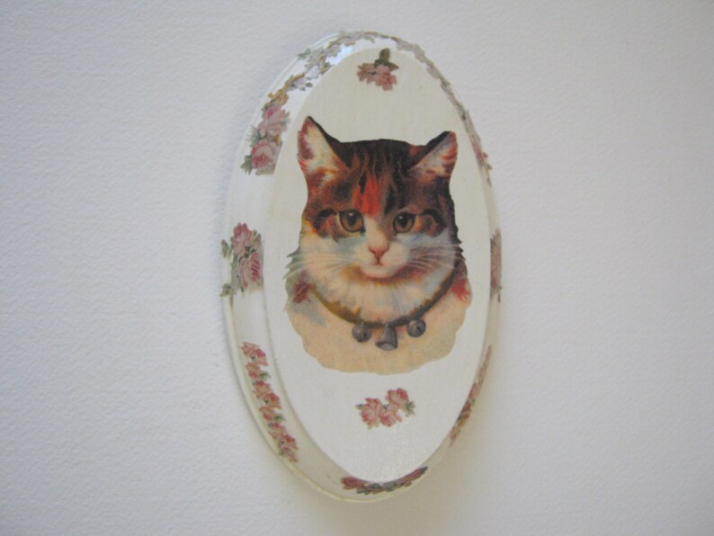 May include: A white oval ceramic plate with a floral design and a vintage image of a cat with brown, black, and white fur.