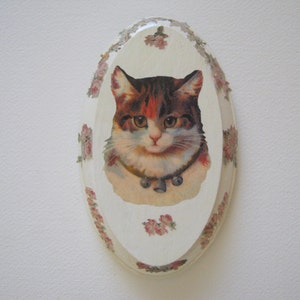 May include: A white oval-shaped ceramic trinket box with a floral design and a picture of a cat with a collar.