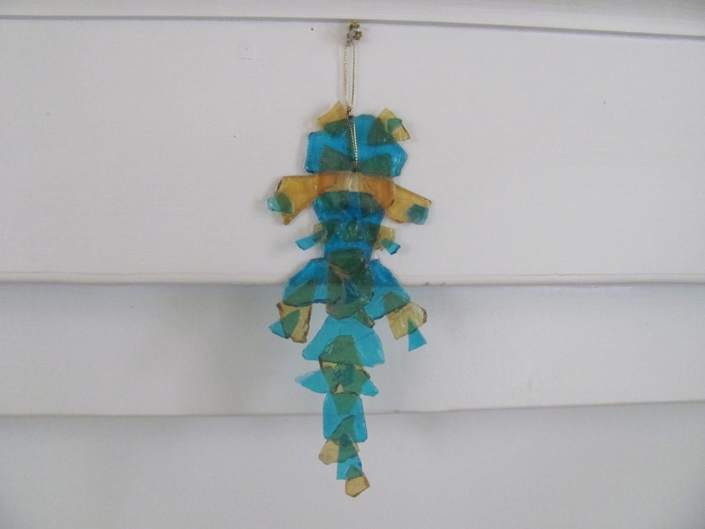 May include: A blue and gold glass ornament shaped like a seahorse. The ornament is made of many small pieces of glass that are glued together.