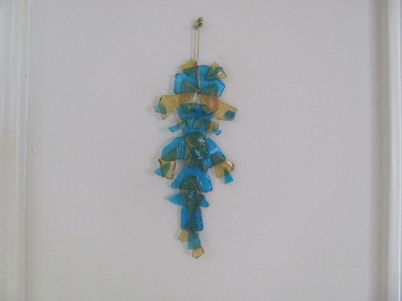 May include: A blue and gold glass mobile with a teardrop shape hangs from a white ceiling.