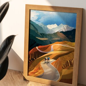 May include: Framed illustration of three cyclists riding on a winding road through a mountainous landscape. The mountains are painted in shades of blue, green, and brown, with snow-capped peaks. The road is paved and curves through the landscape. The cyclists are wearing colourful clothing and riding road bikes.