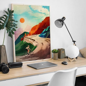 Pu&ograve; includere: Un poster incorniciato con un'illustrazione colorata di un ciclista che sale su una strada di montagna tortuosa. Il cielo &egrave; blu con nuvole bianche e un sole arancione brillante. Le montagne sono verdi, rosse e marroni.